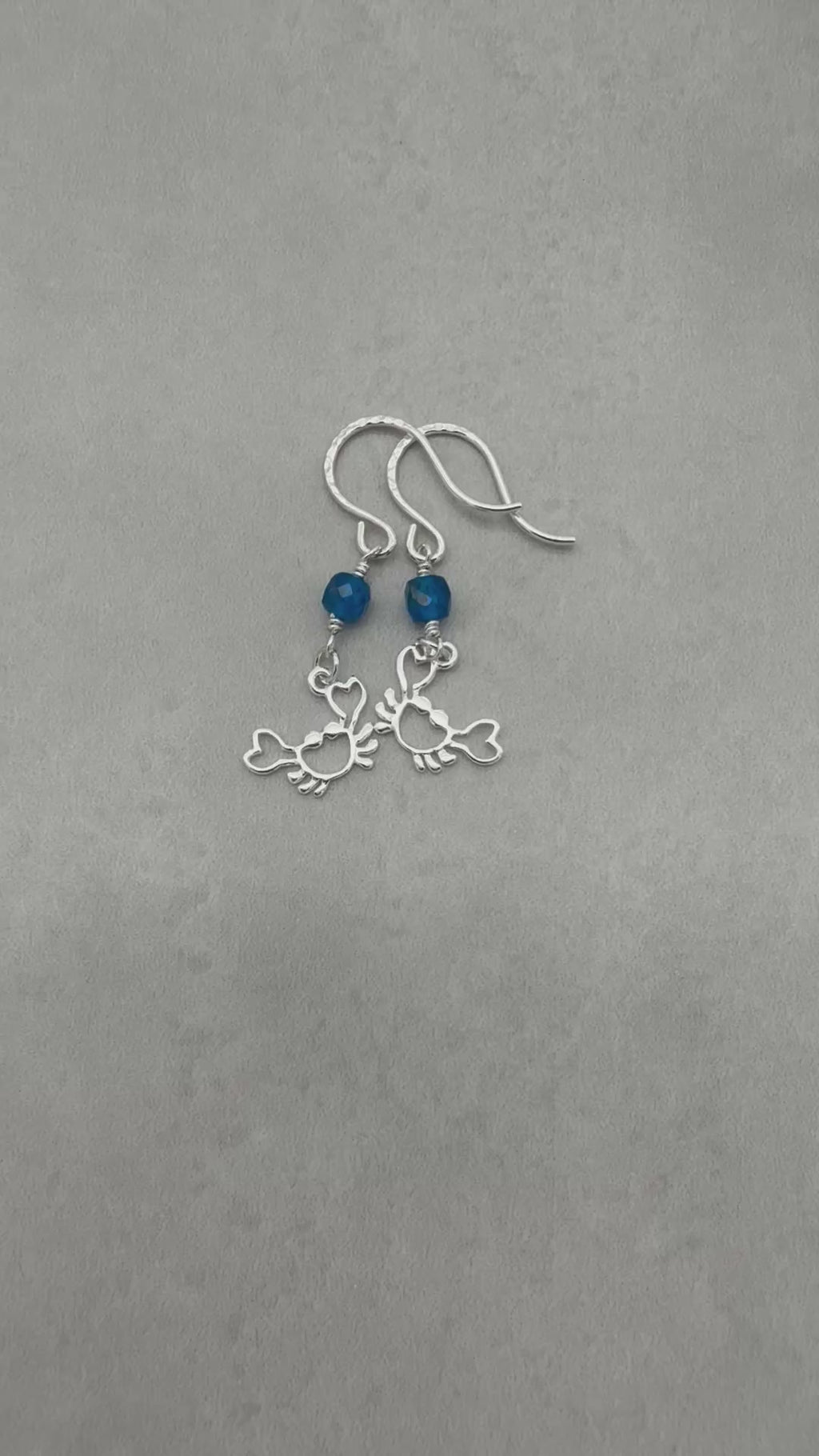 Video of sterling silver dangle earrings with crab charms, apatite, and silver ear wires on a gray surface - handmade with love by Ruby Acorn