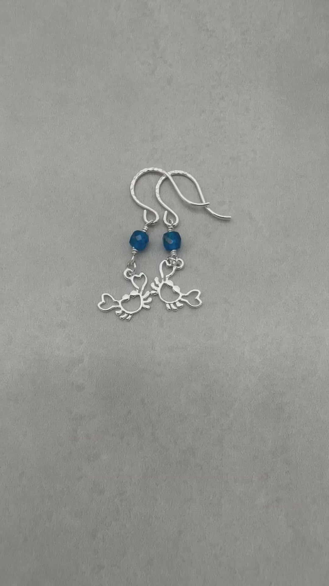 Video of sterling silver dangle earrings with crab charms, apatite, and silver ear wires on a gray surface - handmade with love by Ruby Acorn