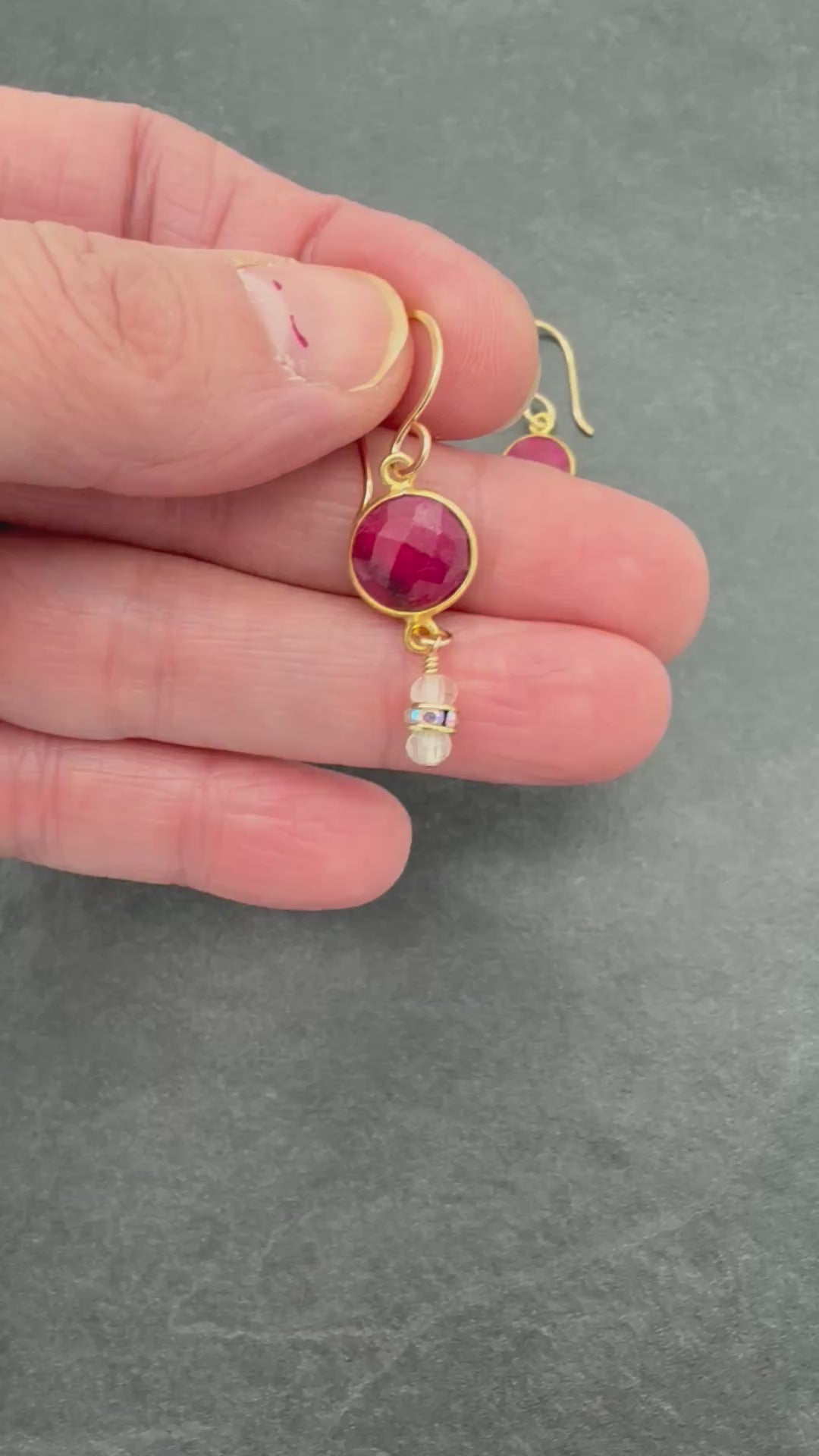Video of hand holding gold earrings with red gemstones and moonstone drops