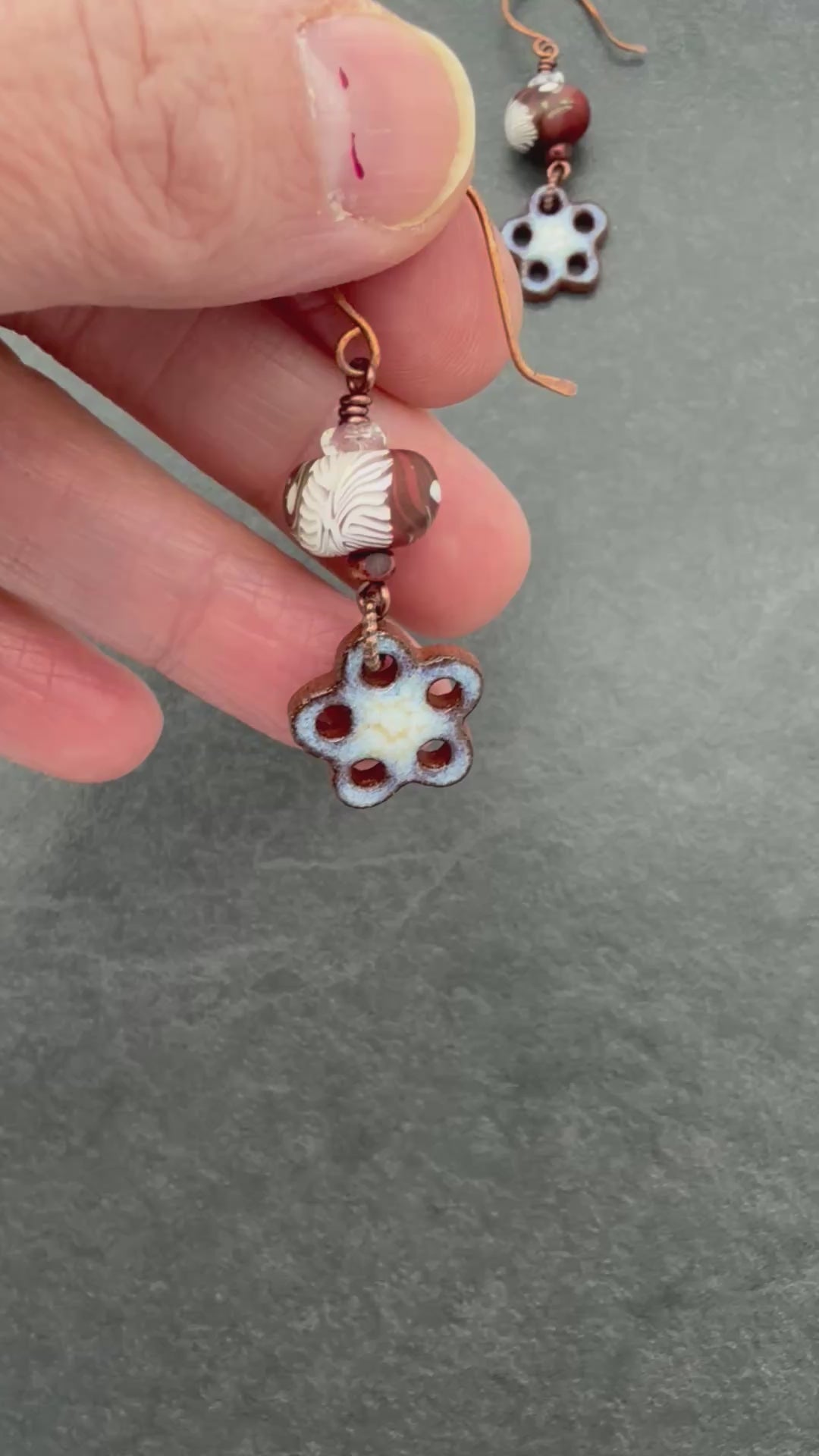 Video of hand holding brown and white earrings