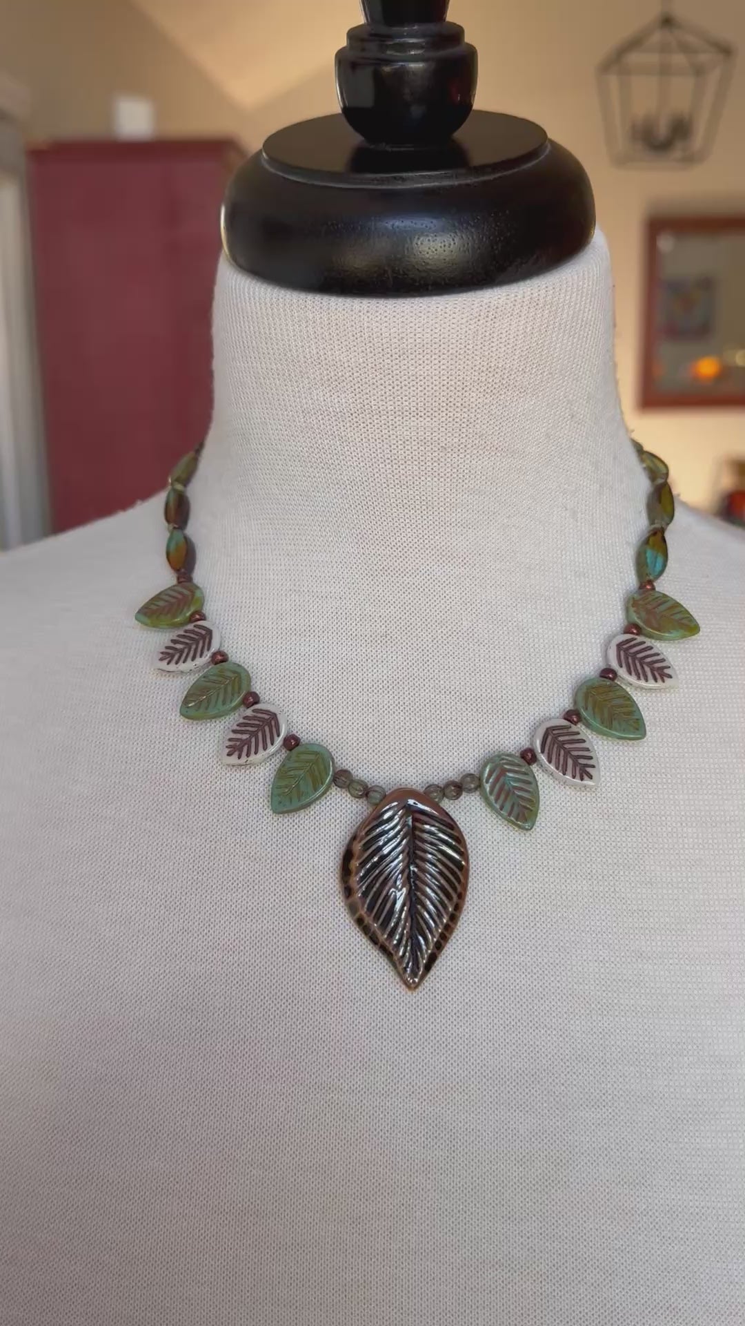 Video of a colorful necklace with a leaf pendant on a bust