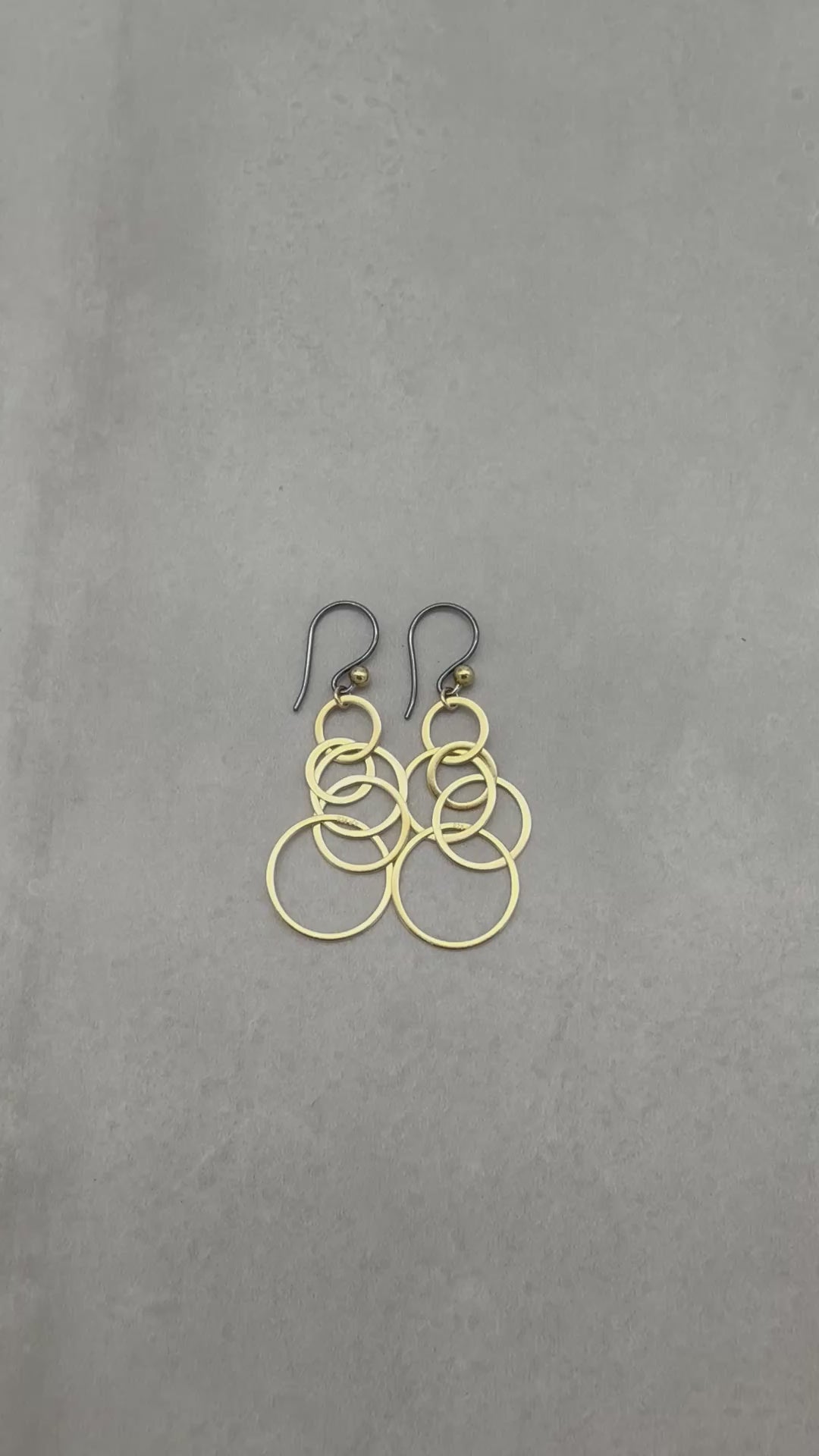 A video of gold interlocking hoop earrings with black silver ear wires on a gray background - made with love by Ruby Acorn.