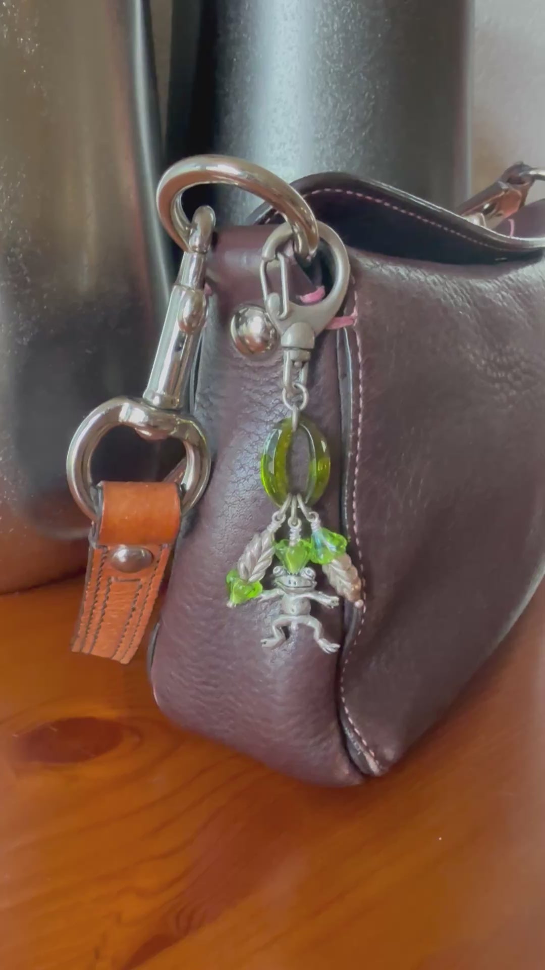 Video of decorative handbag charm with frog charm attached to a brown leather purse.