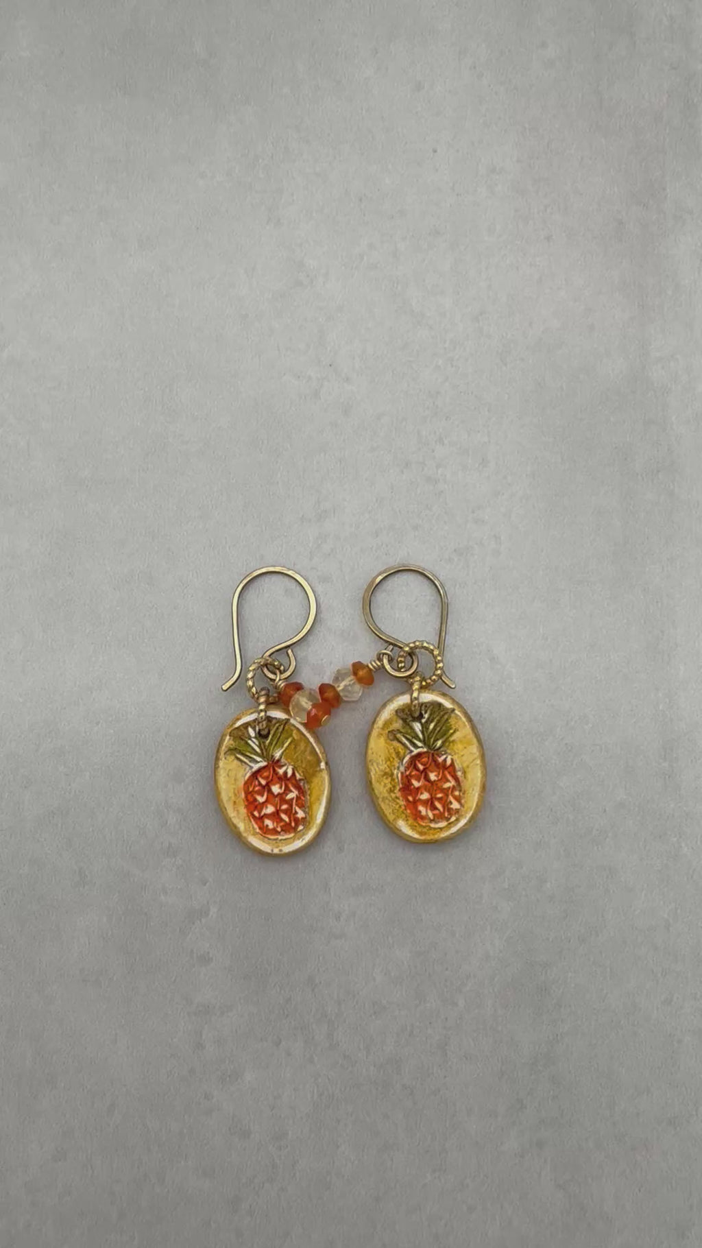 Video of handmade Pineapple charm earrings with brass ear wires on a gray surface - made with love by Ruby Acorn