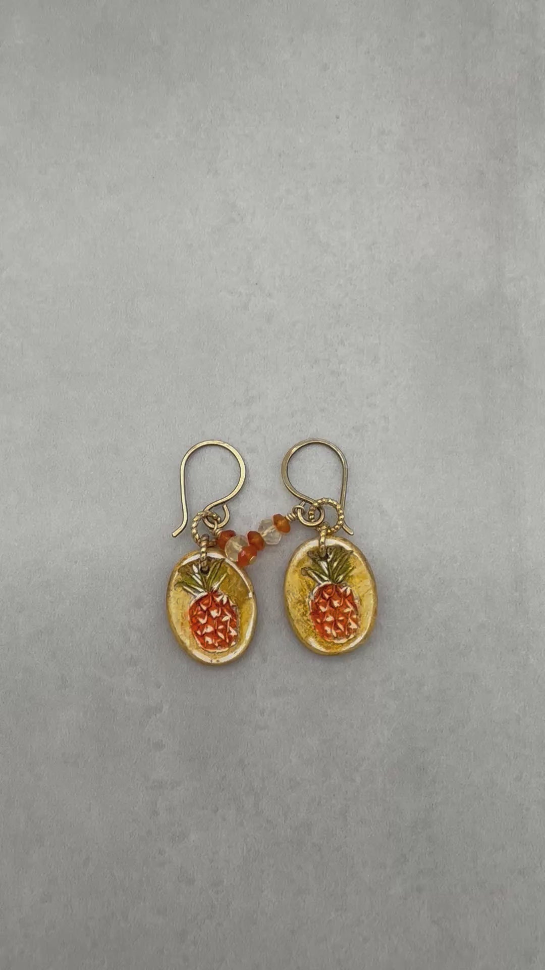 Video of handmade Pineapple charm earrings with brass ear wires on a gray surface - made with love by Ruby Acorn