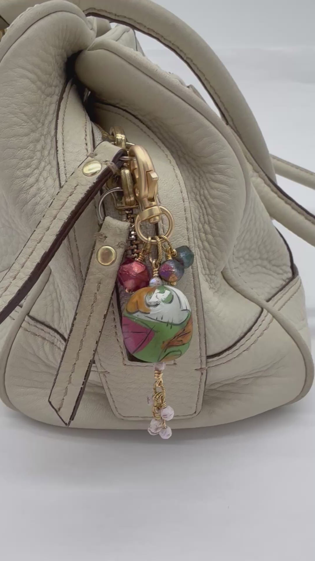 A video of a handmade bag charm with a colorful artisan polymer clay focal and Czech glass beads on a cream leather handbag - made with love in Colorado by Ruby Acorn.