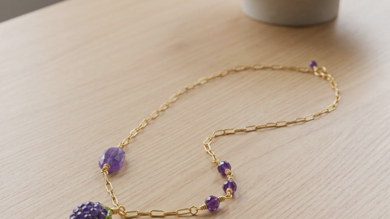 Asymmetrical Blackberry Necklace with artisan lampwork focal and amethyst on a light wood background.